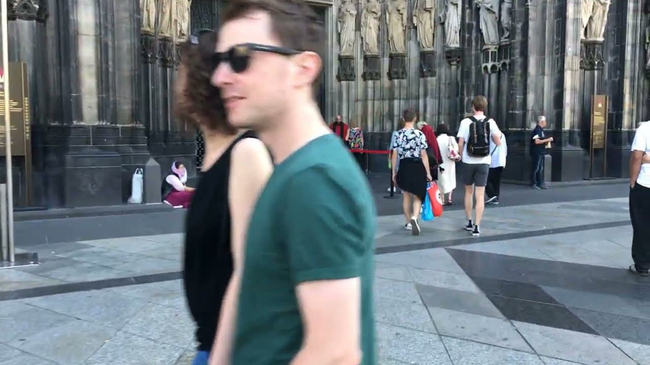 Visitors walking past the Gothic west front of Cologne Cathedral on a sunny day